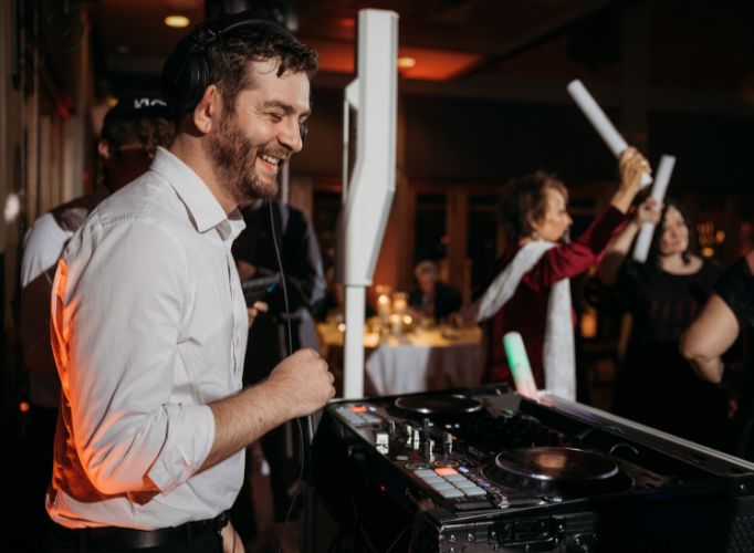 DJ Nick Fortini smiling, having fun at a wedding with guests dancing in background