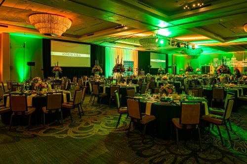 Ballroom set for a gala, bathed in shades of green and yellow with three screens for presenting.