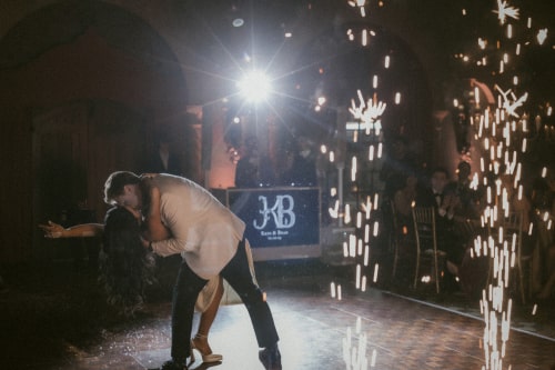 Groom dipping bride during first dance as a cold spark goes off in the background with a flare from main spotlight