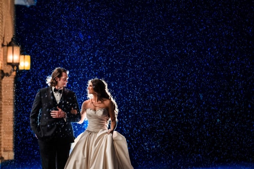 A bride and groom walking as faux snow falls around them
