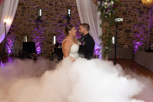 Couple dancing on empty dance floor with purple accent lighting in a sea of faux, fog clouds