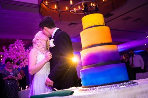 A couple sharing a kiss with their spotlighted cake accenting the right of the image